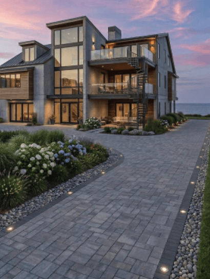 Modern coastal home with a paver driveway lined by warm in-ground path lights at dusk