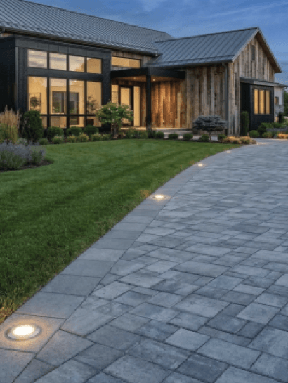 Modern black-and-timber home beside a wide paver driveway picked out by in-ground lights at dusk