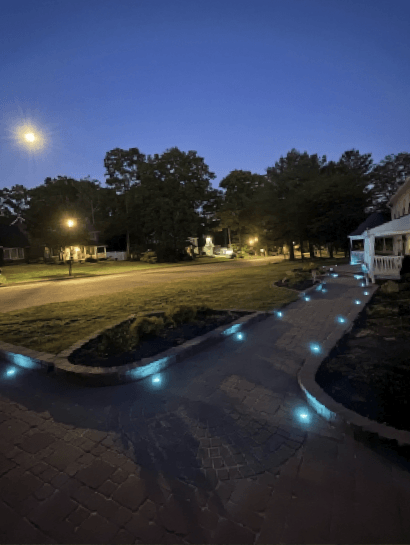 Paver driveway and walkway traced by cool-toned in-ground lights on a clear moonlit night